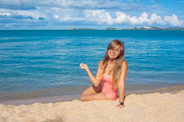 Uśmiechnięta młoda kobieta w strój kąpielowy różowy, siedząc na tropikalnej plaży — Zdjęcie stockowe