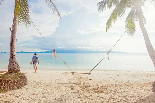 Muž na tropické pláži za houpačky mezi kokosovými palmami — Stock fotografie
