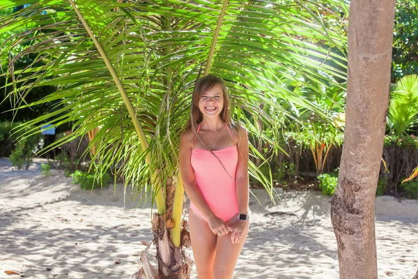 Menina engraçada em maiô rosa em pé na praia tropical perto da palma verde — Fotografia de Stock