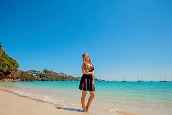 Piękna młoda kobieta z długimi włosami w czarnej sukni stojącej na piasku w pobliżu morza — Zdjęcie stockowe