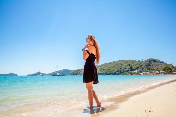 Piękna młoda kobieta z długimi włosami w czarnej sukni stojącej na piasku w pobliżu morza — Zdjęcie stockowe