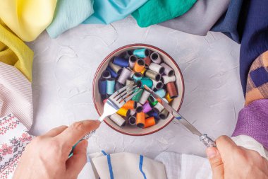 Adam kumaş çok renkli çerçeve iplik makaraları ile kase altında çatal ve bıçak tutar