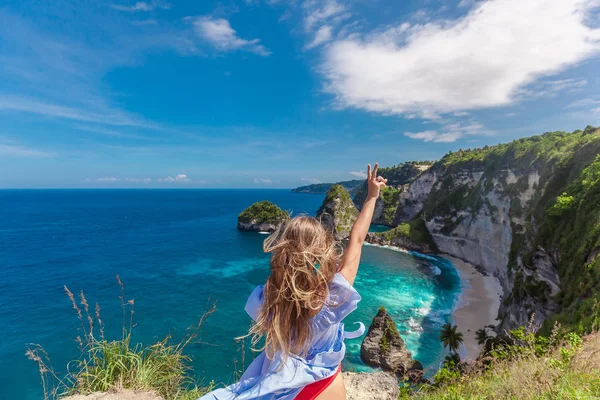 Jonge vrouw opgevoed haar hand in prachtige rots kustlijn in Thousand Island op Nusa Penida, in de buurt van Bali, Indonesië — Stockfoto
