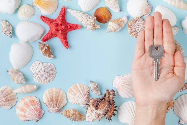 Womens hand hold a key on a blue summer background with different shells and starfish — Stock Photo, Image