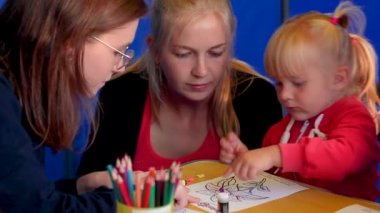 Mutlu genç anne ve öğretmen resim üzerinde sopa kağıt ile çocuk kızı yardım
