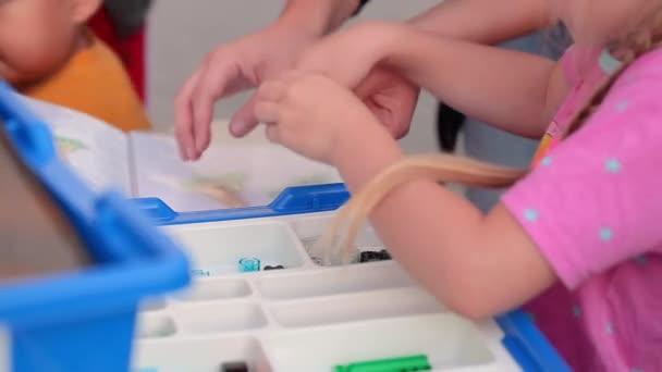 Niña con la ayuda de un maestro hace una figura de lego cubos — Vídeo de stock
