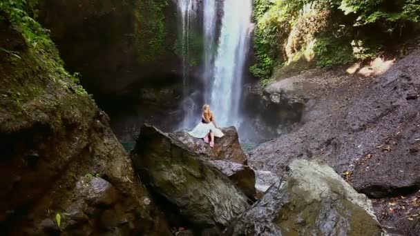 Młoda kobieta siedzi na kamieniach przed wodospad Bali Aling-aling — Wideo stockowe