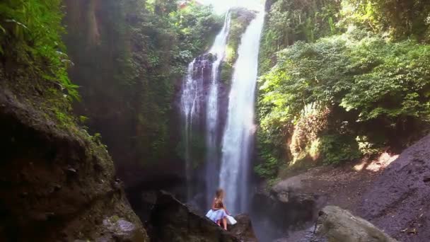 Mujer joven sentada en las rocas frente a la cascada de Bali Aling-aling — Vídeo de stock