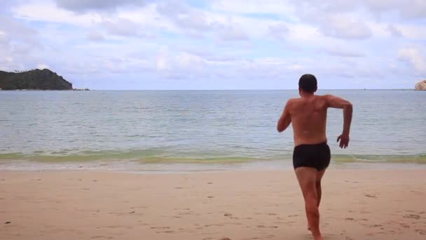 Hombre divertido corriendo en la playa hacia el mar, saltando al mar y nadando — Vídeo de stock