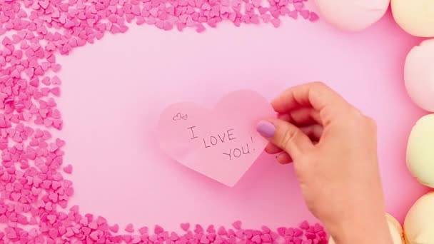 Mão feminina colocando um cartão valenines com eu amo você assinar no fundo rosa — Vídeo de Stock