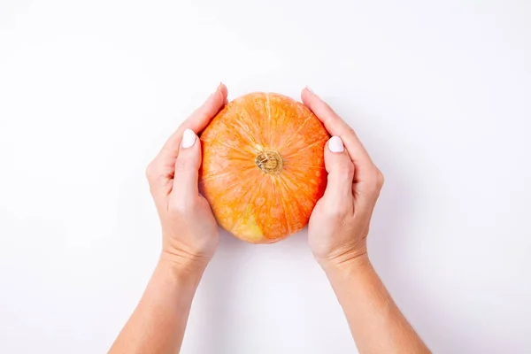 白い背景に小さなオレンジ色のカボチャを持つ女性の手。トップビュー — ストック写真