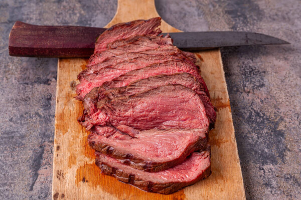 Roast beef slices on wooden cutting board with old knife on marble background. Gourmet food. Raw meat beef steak. Chopped roast beef with pink juice