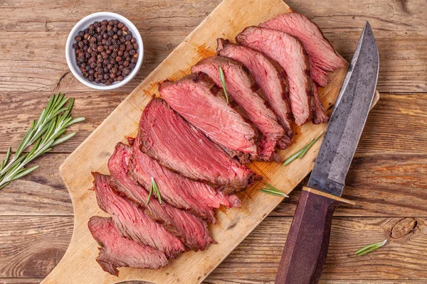 Sliced medium rare roasted beef meat on wooden cutting board, hunters knife — Stock Photo, Image