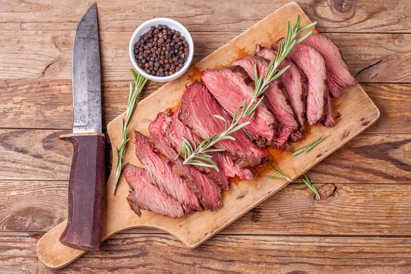 Sliced medium rare roasted beef meat on wooden cutting board, hunters knife — Stock Photo, Image