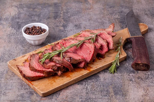 Fette di roast beef medio raro su tagliere di legno, coltello vecchio, pepe — Foto Stock