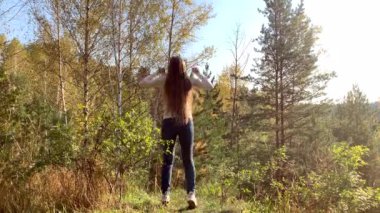 Uzun saçlı mutlu genç kadın atlar ve ormanda bir galibiyet gibi ellerini kaldırır