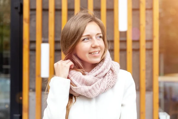 Smiling young businesswoman in white coat with scarf near the office building