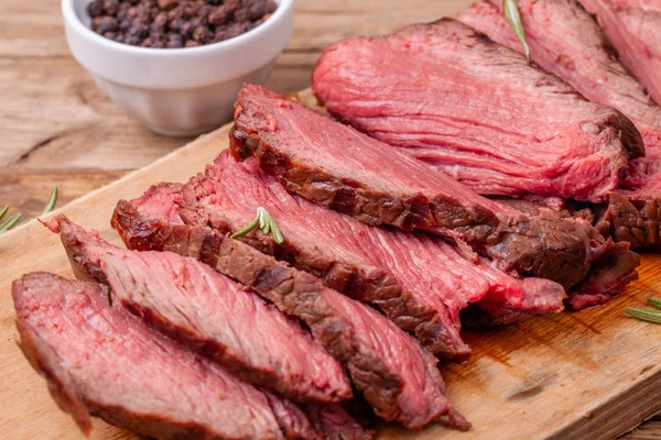 Close up slices of medium rare roast beef on wooden cutting board with rosemary — Stock Photo, Image