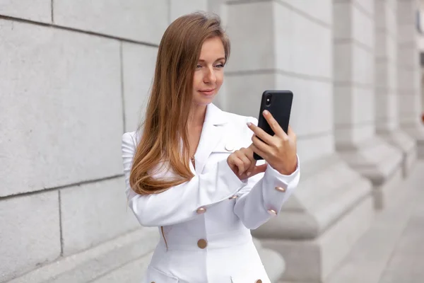 Femme d'affaires heureuse tenant et touchant le smartphone près de l'immeuble de bureaux — Photo