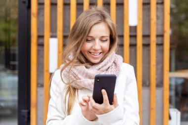 Smiling young woman outside the office holding and using the mobile phone