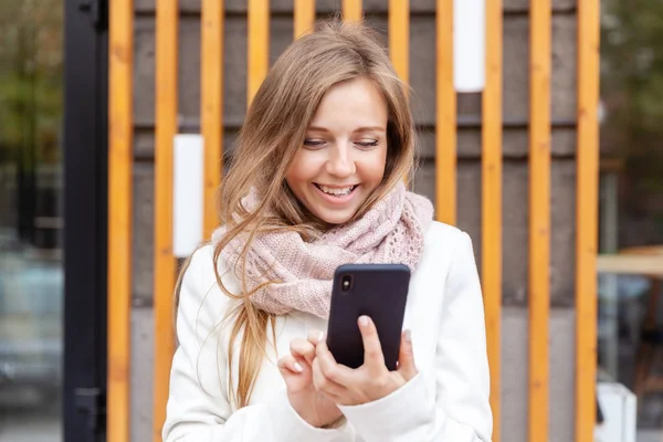 Jeune femme souriante devant le bureau tenant et utilisant le téléphone portable — Photo