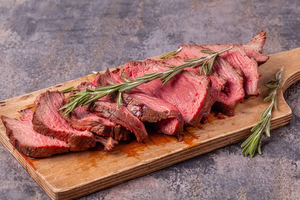 Slices of medium rare roast beef meat on wooden cutting board and rosemary twigs — Stock Photo, Image