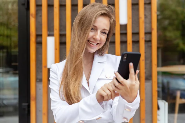 Portrait de heureuse jeune femme d'affaires souriante aux cheveux longs utilisant un smartphone — Photo