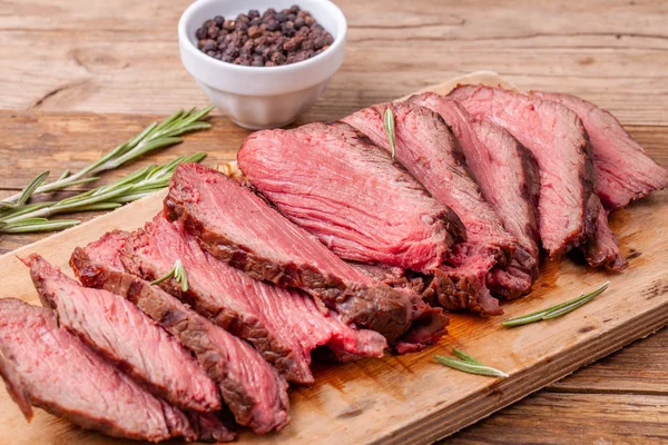 Close up slices of medium rare roast beef on wooden cutting board with rosemary — Stock Photo, Image