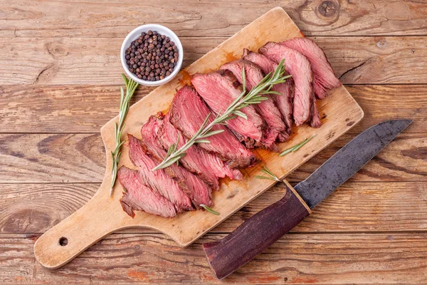 Slices of medium rare roast beef meat on wooden cutting board, hunters knife — Stock Photo, Image