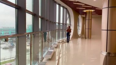 Mutlu gülümseyen genç bir kadın cep telefonuyla konuşuyor, ofis binasında yürüyor.