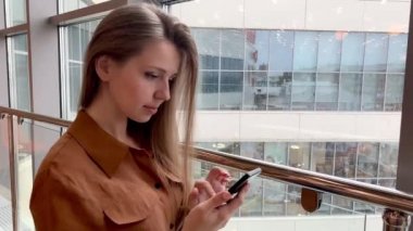 Ofisin içinde akıllı telefondan bakan gülümseyen genç iş kadınının yakın çekimi.