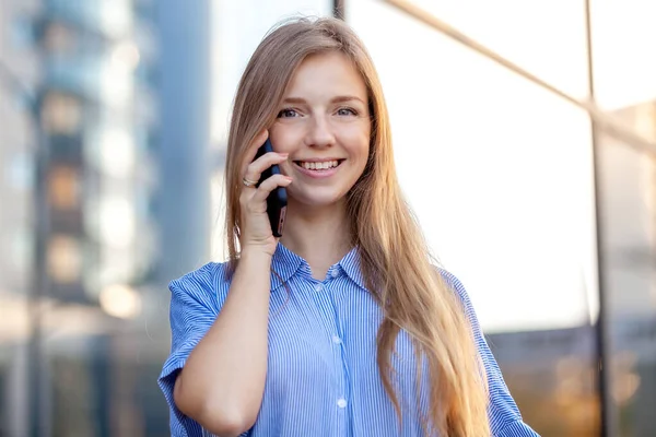 Heureuse femme souriante qui parle sur son téléphone portable et regarde la caméra en face du bureau — Photo