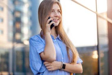 Ofis pencerelerinin yanında cep telefonuyla konuşan mutlu, güzel genç bir kadın.