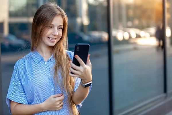 Feliz sonrisa joven atractiva utilizando un teléfono inteligente cerca del edificio de oficinas — Foto de Stock