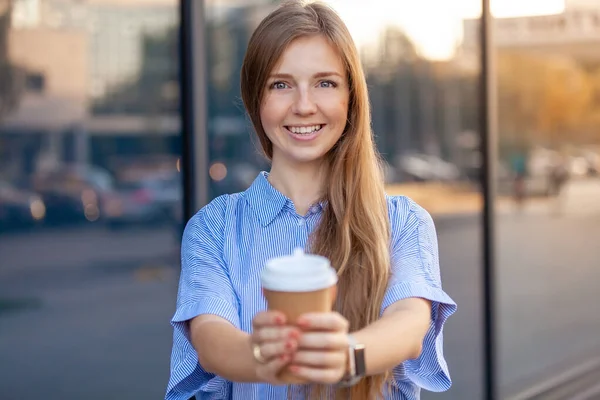 Mujer joven feliz sonriendo a la cámara que ofrece café en taza de papel desechable — Foto de Stock