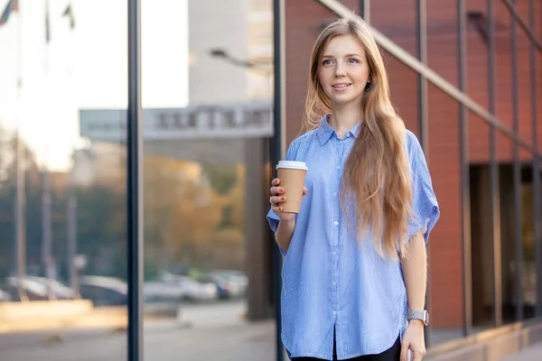 Mujer joven y feliz sosteniendo un café en una taza desechable, caminando por el edificio — Foto de Stock