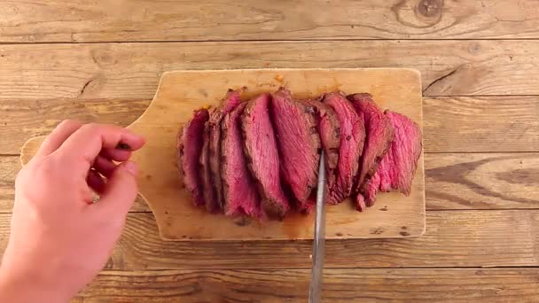 Man hand flips pieces of sliced grilled medium rare roast beef by hunters knife — ストック動画