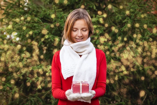 Happy young woman with Christmas gift box on hands with golden lightning bokeh