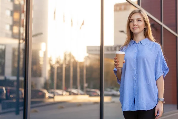 Joyeux jeune femme tenant un café pour aller dans une tasse jetable, marchant le long du bureau — Photo