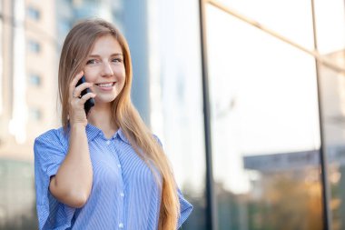 Ofisin karşısında cep telefonuyla konuşan mutlu ve çekici bir kadın var.