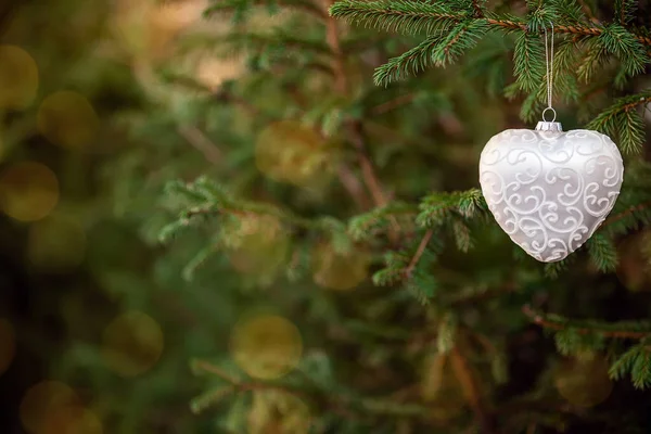Christmas decoration toy shaped like heart hanging on fir tree with bokeh lights — Stock Photo, Image
