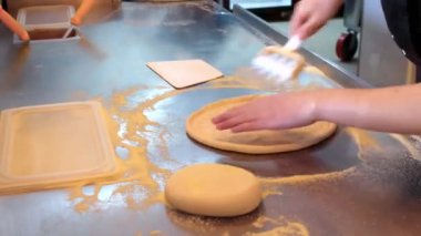Pizzacı, restoranın mutfağında hamur hazırlayıp hamura delik açıyor.