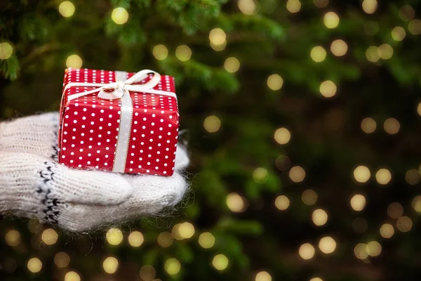 Close-up handen in gebreide wanten met kerst geschenkdoos op bokeh achtergrond — Stockfoto