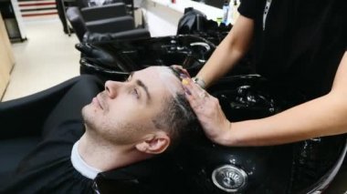 Sakallı adam berber dükkanındaki kuaförün ellerinden saç yıkar.