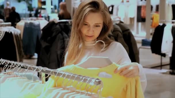 Молода приваблива щаслива жінка покупки одягу в модному магазині одягу — стокове відео