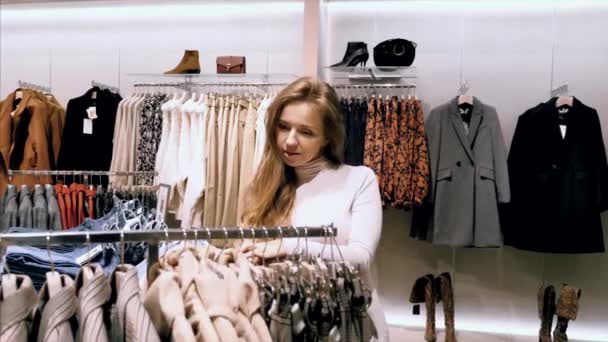 Молодая привлекательная счастливая женщина покупает одежду в магазине одежды в торговом центре — стоковое видео