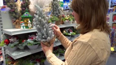 Olgun beyaz kadın alışveriş merkezinde küçük yapay Noel ağacını seçiyor.