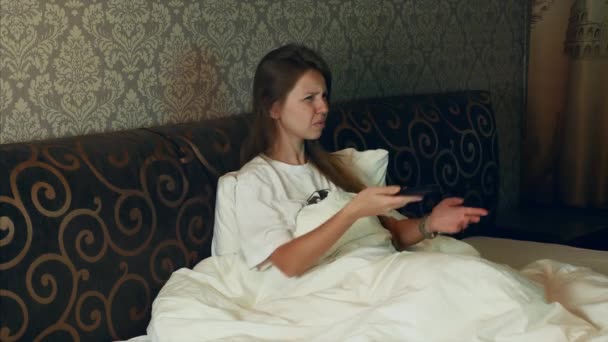 Angry upset woman watching, talking and screaming on tv while sitting on a bed — Stockvideo