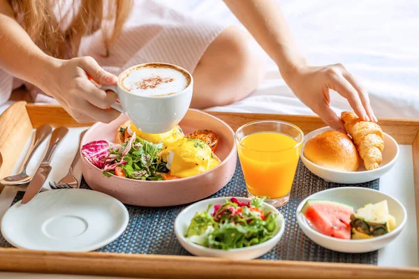 Frukost på sängen med kaffe, apelsinjuice, sallad, frukt och ägg Benedict — Stockfoto