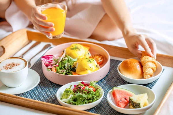 Frukost på sängen med kaffe, apelsinjuice, sallad, frukt och ägg Benedict — Stockfoto